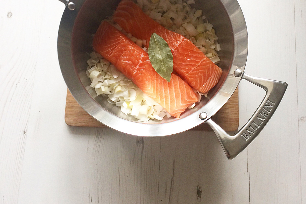 A saucepan of chopped leeks with salmon and a bay leaf on top