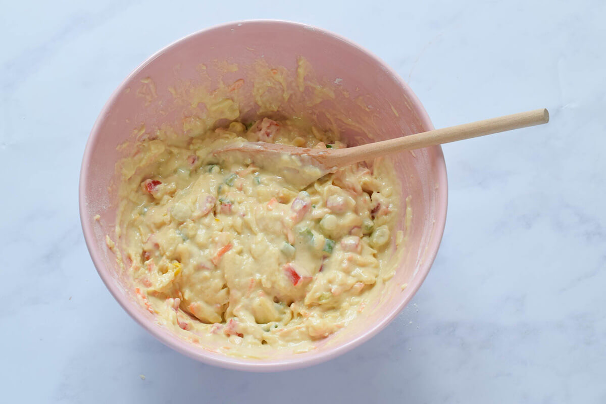 A bowl of flour with grated carrot, chopped spring onion, red pepper and sweetcorn mixed with milk, egg and olive oil