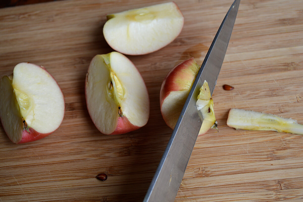 A chopping board with a quartered apple having the seed core cut out