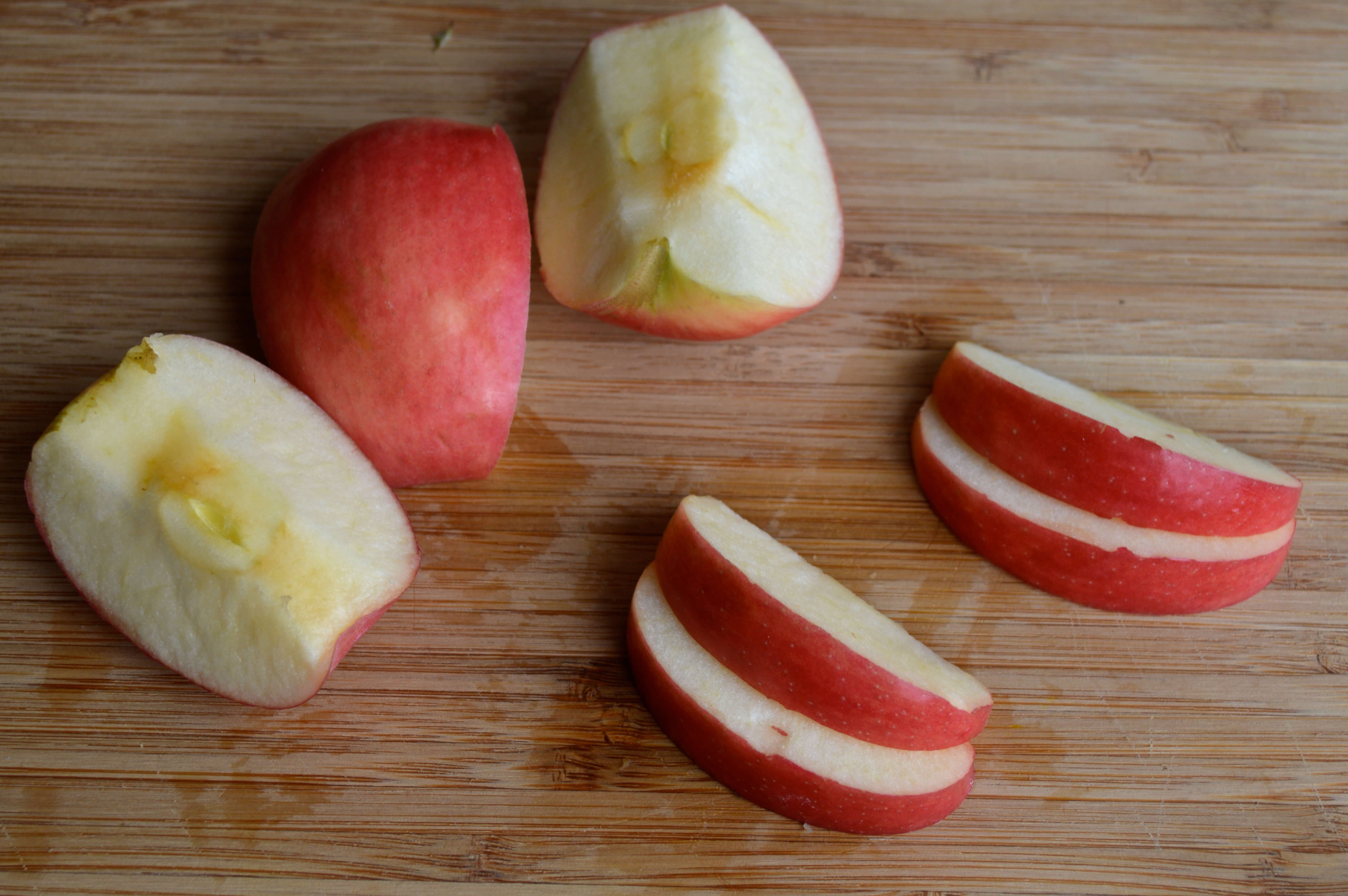 A chopping board with some quartered apples next to some apple slices/wedges