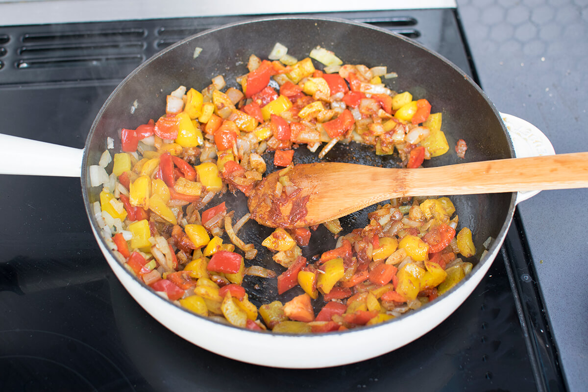 A frying pan of onion, garlic, peppers, herbs, spices and tomato paste