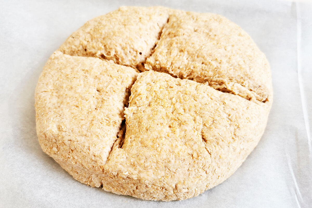 Soda bread dough on a baking sheet with a cross cut across the centre