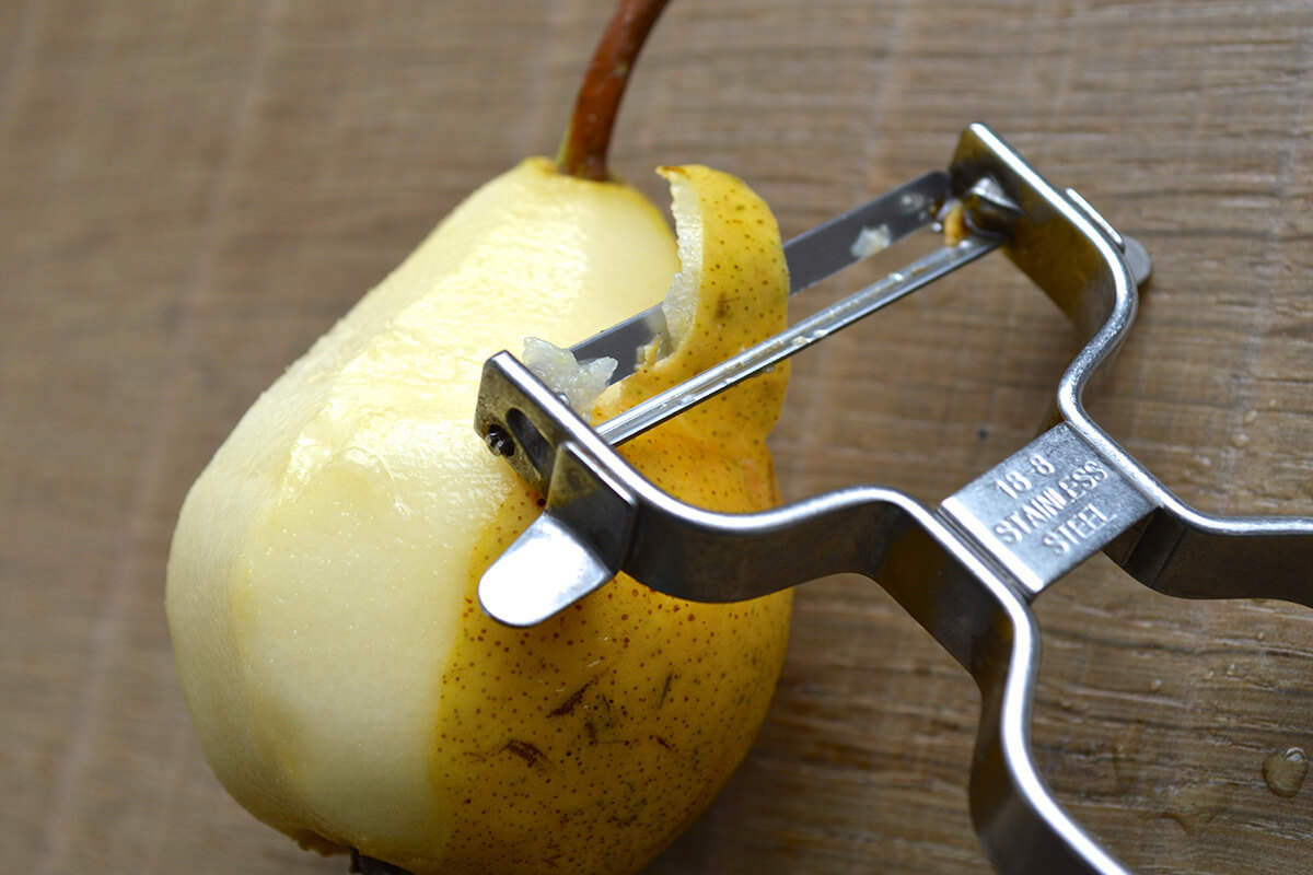 A whole pear being peeled with a metal peeler