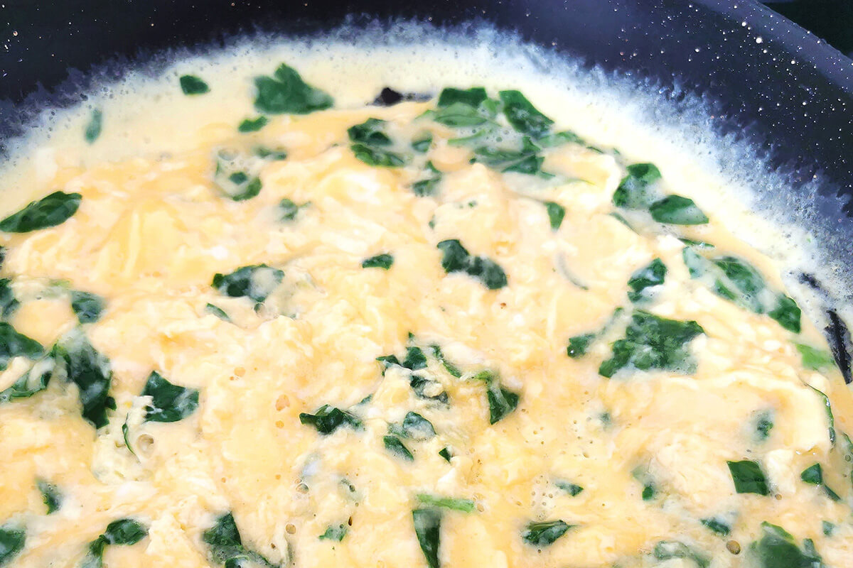 Spinach omelette being cooked in frying pan 