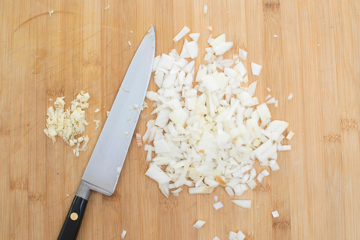 Chopped onion and crushed garlic on a wooden chopping board