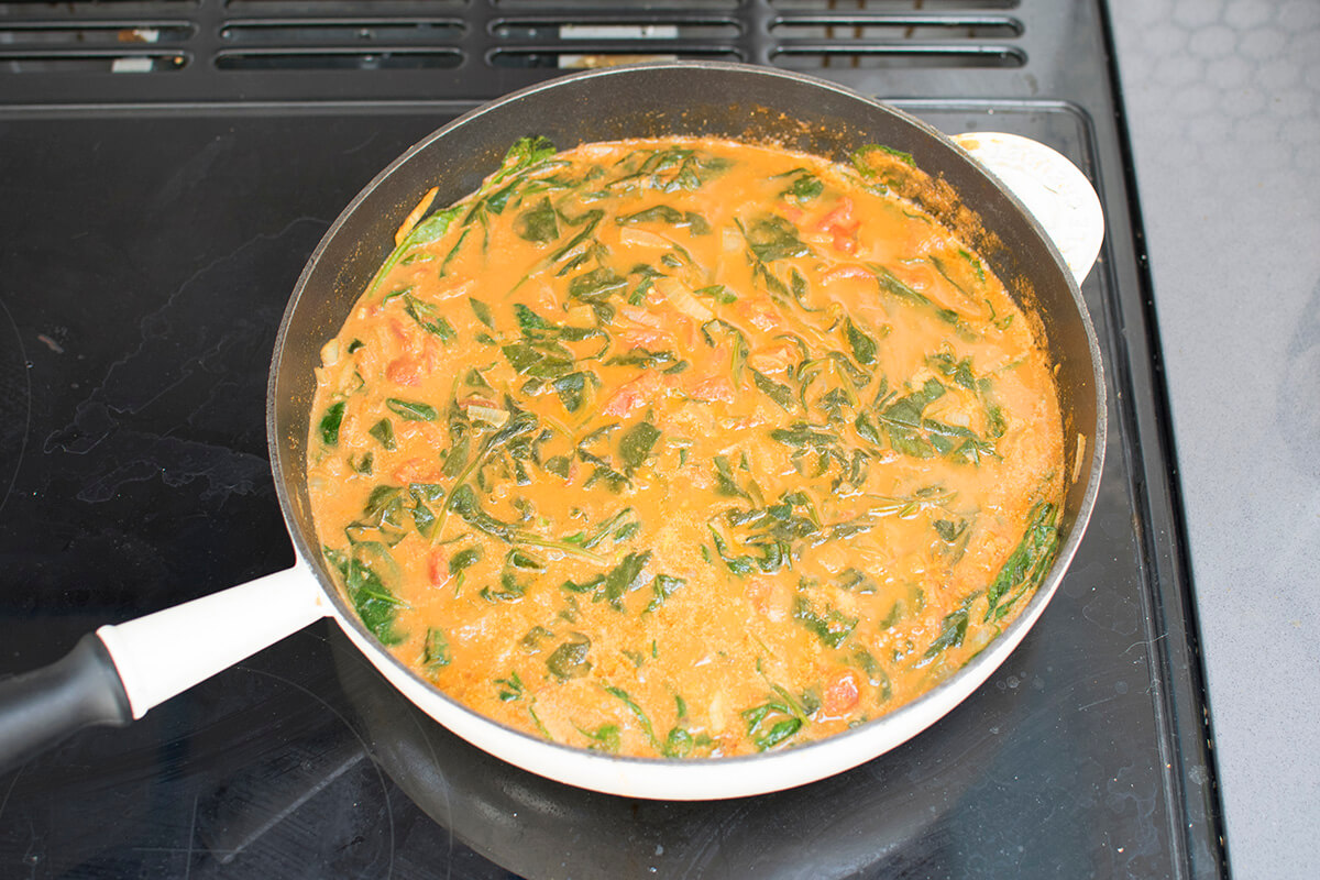 A saucepan with chopped tomatoes, coconut milk, stock and spinach, drained chickpeas and lemon juice