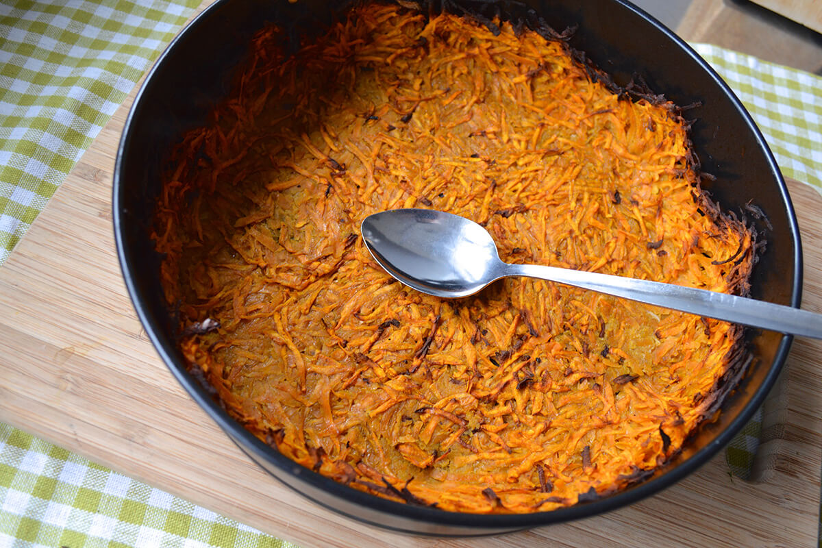 A tart tin with cooked sweet potato crust in it, being smoothed over with the back of a spoon