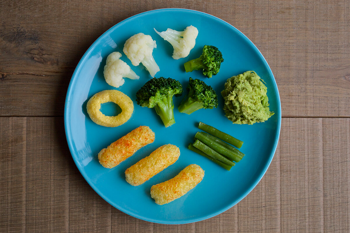 3 organix melty carrot puffs, an oranix melty sweetcorn ring, 3 broccoli florets, 3 cauliflower florets, 6 fine green beans and 1 quarter of a mashed avocado on a plate