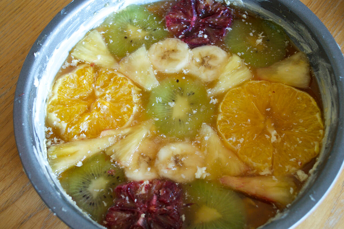 Buttered cake tin with orange, blood orange, kiwi, banana and pineapple chunks pressed into it