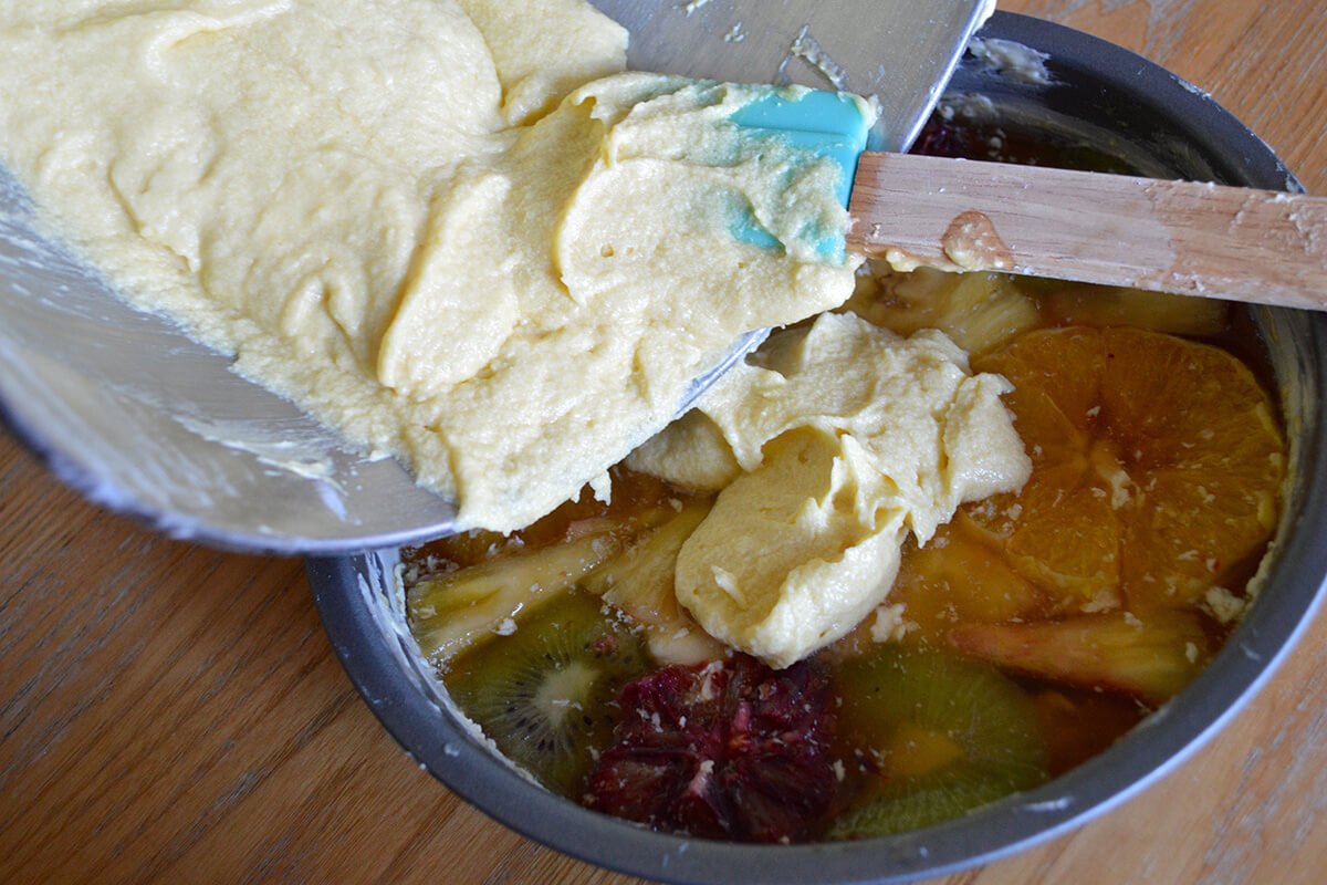 Cake batter being poured over the fruity layer in the buttered cake tin