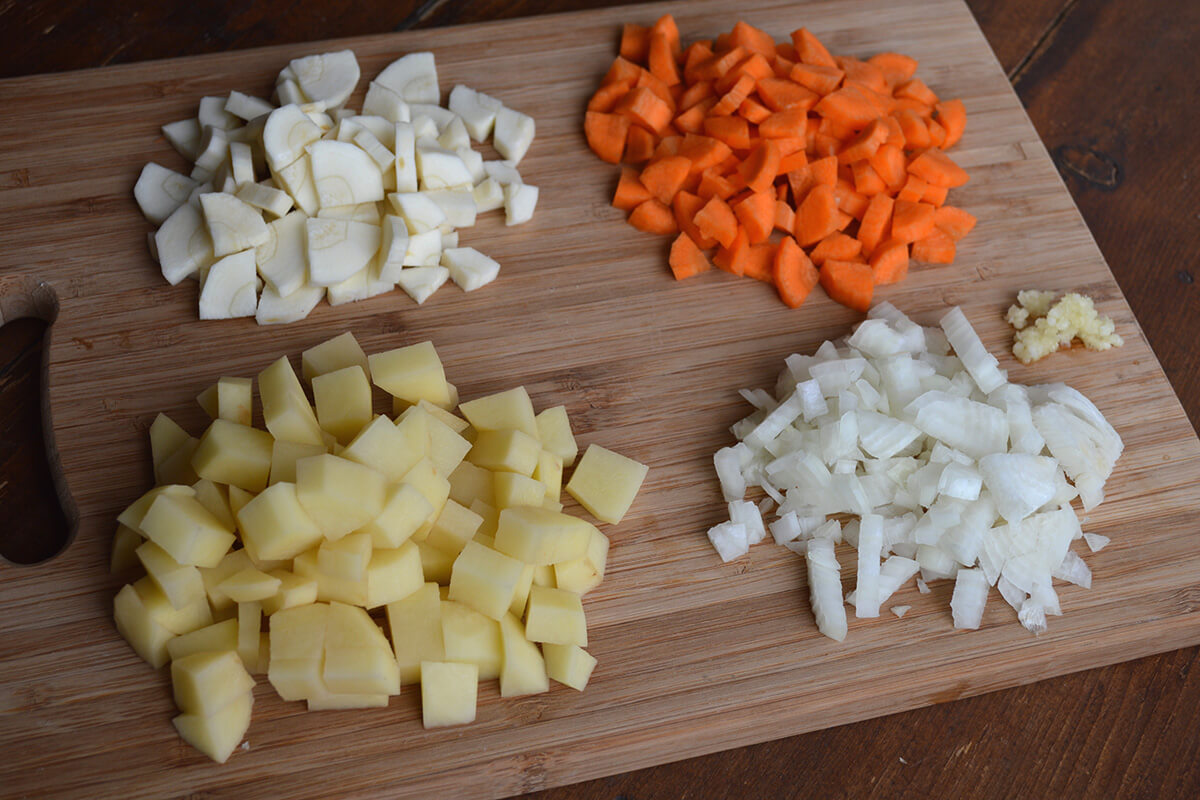 A chopping board with chopped onion, potato, carrot, parsnip and garlic