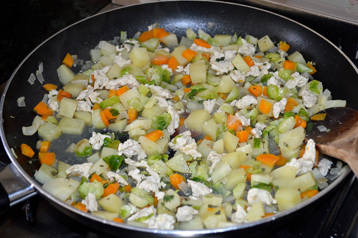 A frying pan with onion, garlic, potato, carrot, parsnip and turkey 