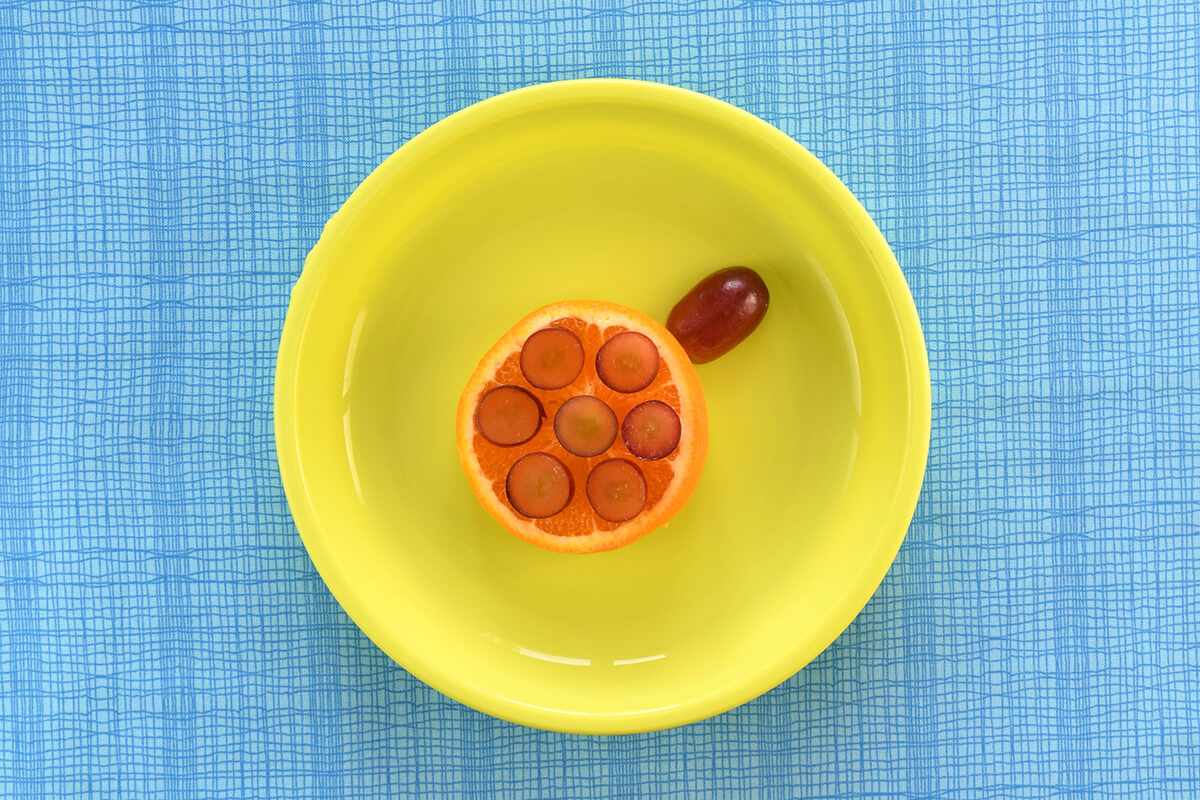 Grape slices arranged on top of the orange slices to create a turtle shell. Half a sliced grape is placed on the oranges to create a head