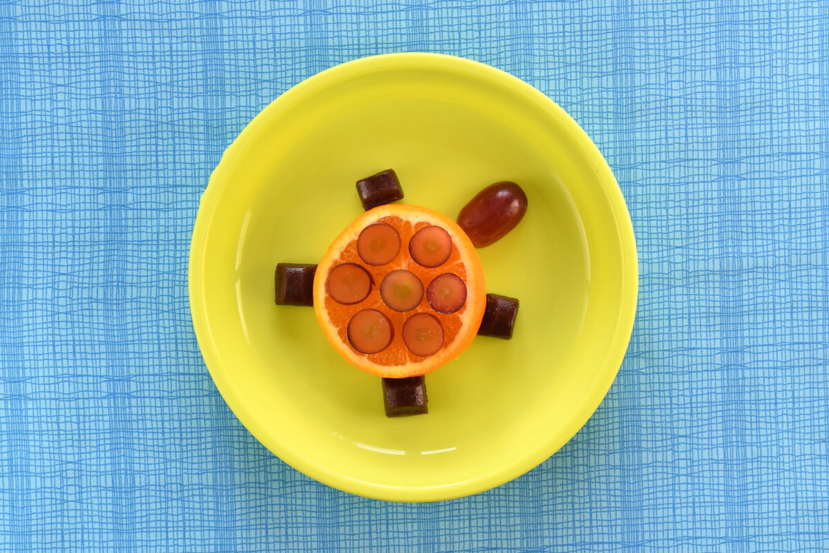 An organix fruit bar is cut into chunks and placed around the orange to create the turtle's legs
