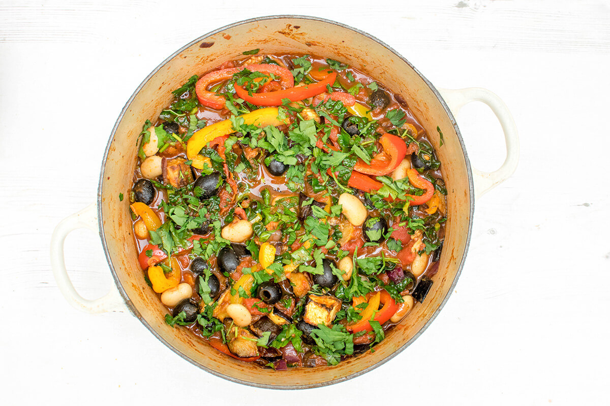 A saucepan of vegetarian bean stew topped with chopped parsley leaves