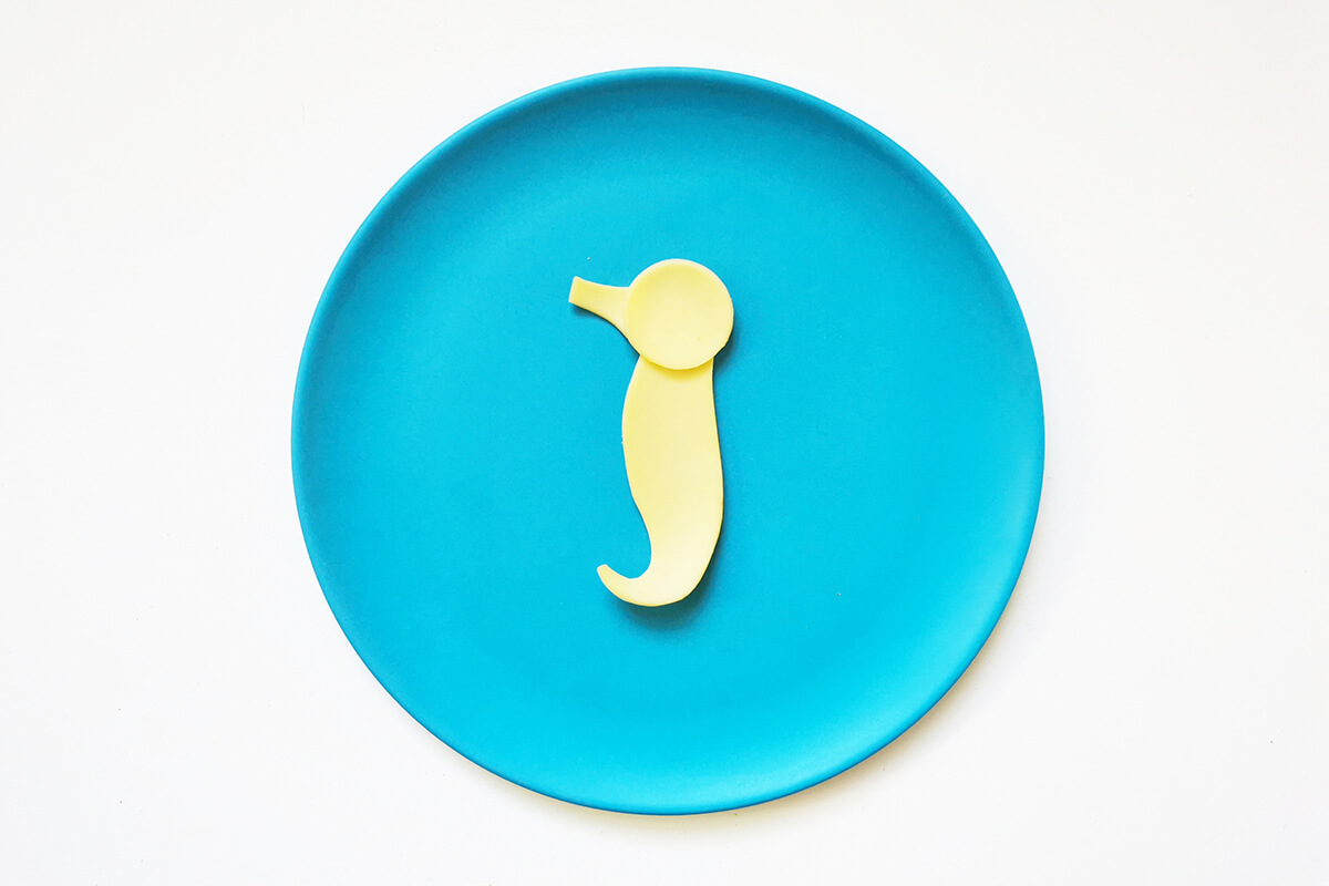 Cheese shapes placed on a plate in the shape of a seahorse. A rectangular shape with a curled end makes the body, a circle with a small rectangular shape make the head and snout