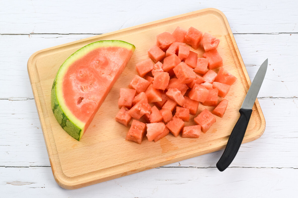 A wooden chopping board with a wedge of watermelon and some cubed watermelon chunks