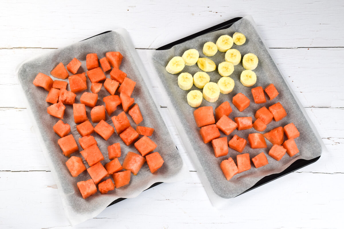 2 lined baking trays with watermelon chunks and banana slices on