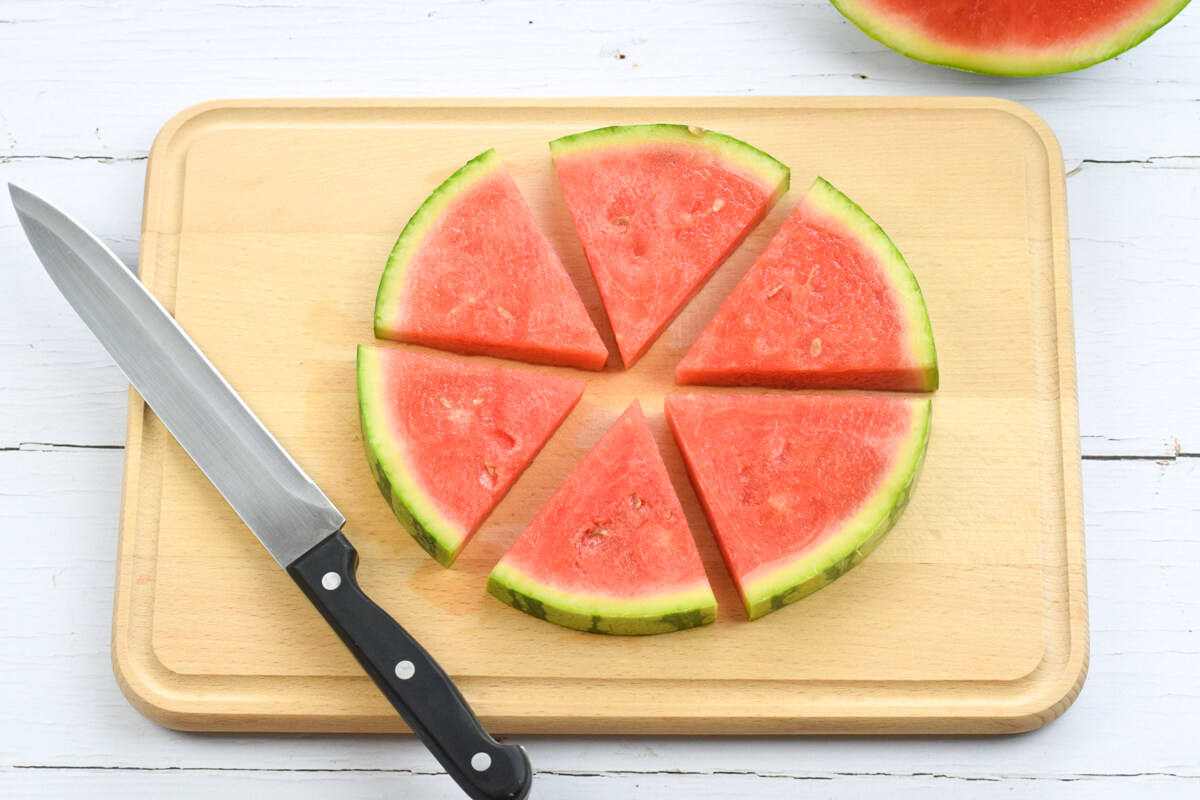 A wooden chopping board with a watermelon round cut into 6 triangle shaped segments