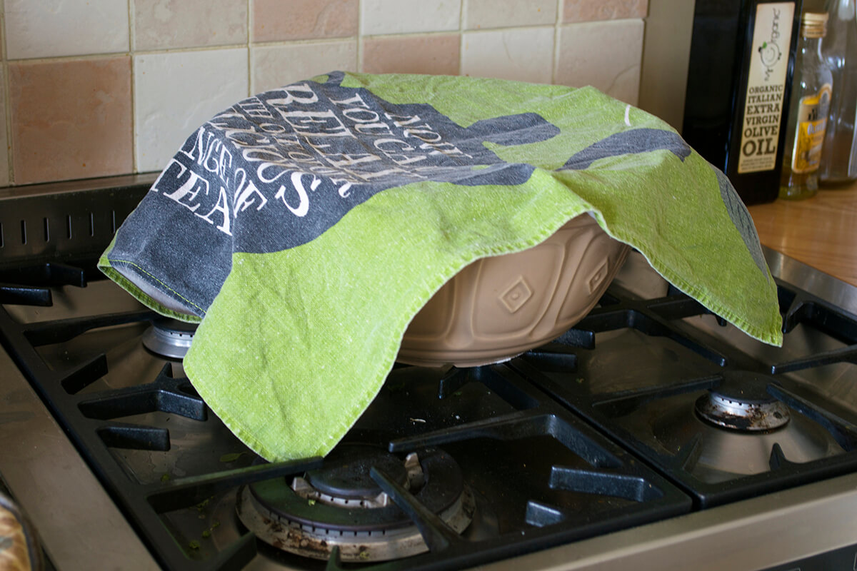 Bread dough resting in a large bowl covered by tea towel 