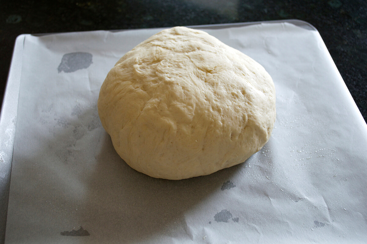 A ball of risen bread dough on parchment paper on a baking tray