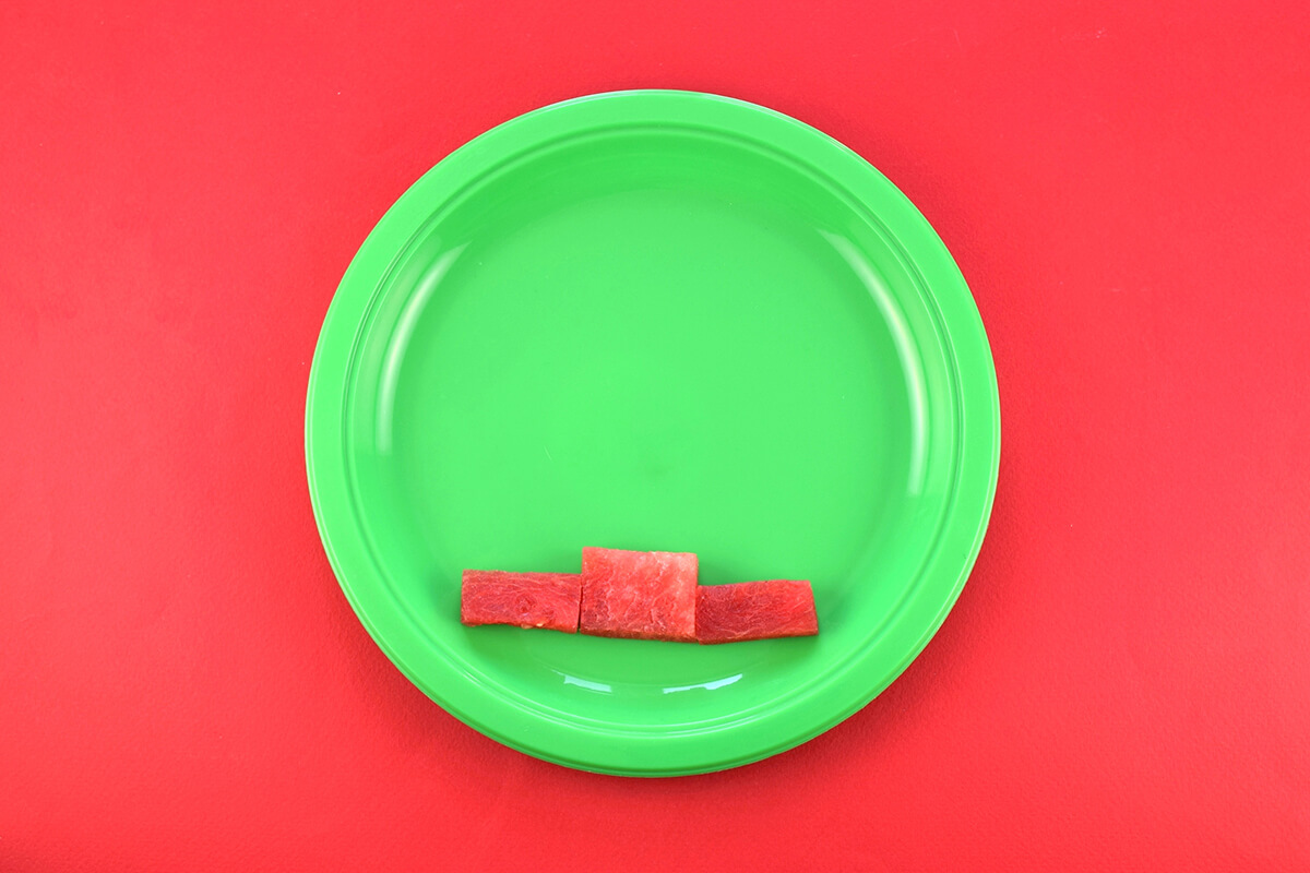3 watermelon pieces arranged in a row at bottom of plate to form a winner's podium, the larger piece of watermelon is in the middle