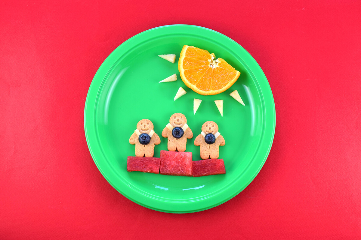 3 organix mini gingerbread men are placed on the watermelon podium with tiny rectangles of apple as medal straps and half a blueberry for the medal