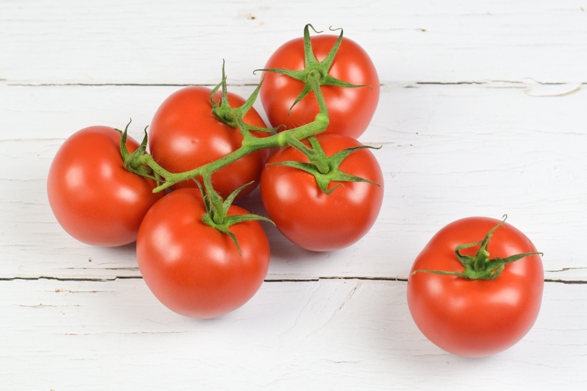 A table with 5 tomatoes on a vine and a whole tomato next to them