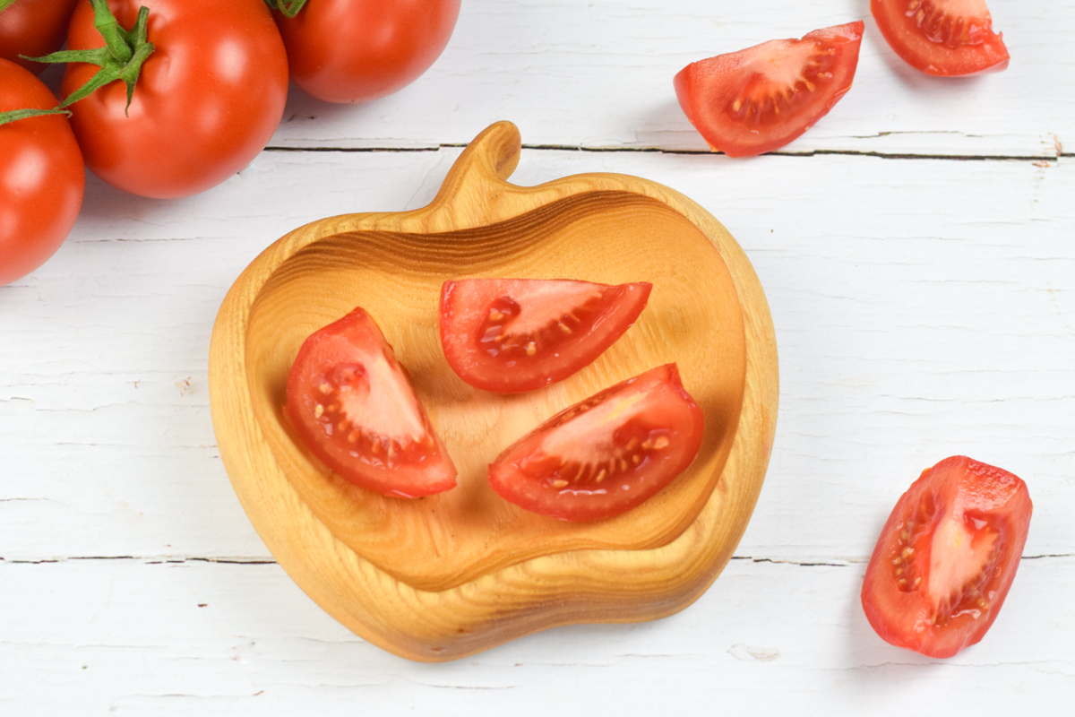 A bowl of tomato wedges next to 3 segments of tomatoes and some whole tomatoes on a vine