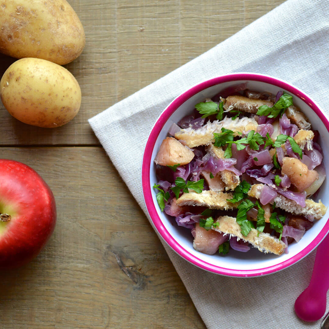 A small bowl of Slow Cooked Red Cabbage & Pork next to an apple and 2 potatoes