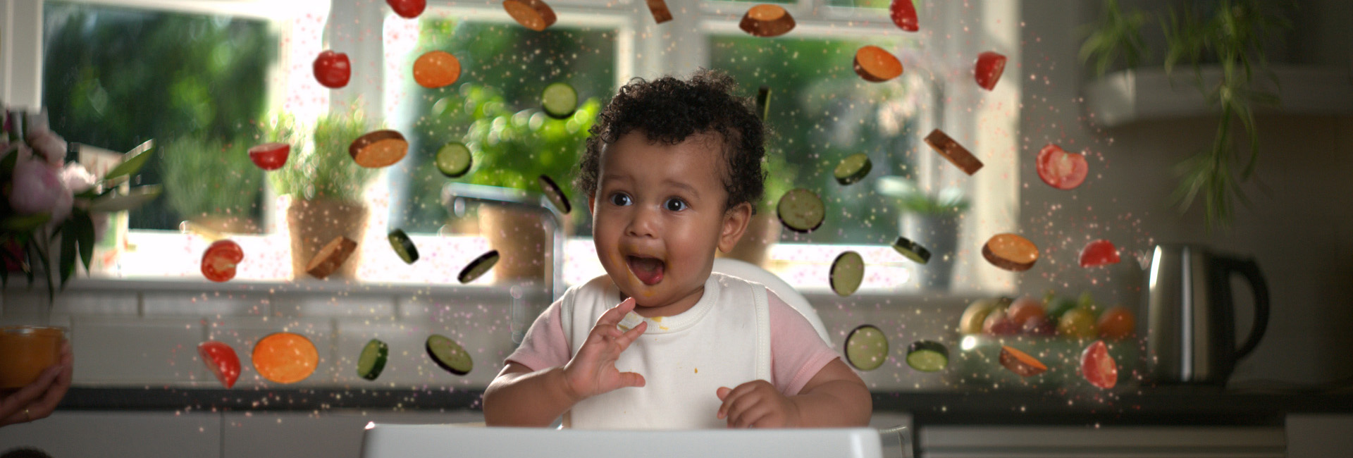 Baby eating a meal on a highchair with a rainbow of vegetables around their head