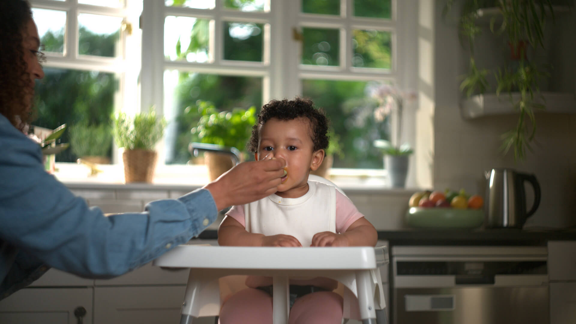 Baby on a highchair in the kitchen with mum feeding them