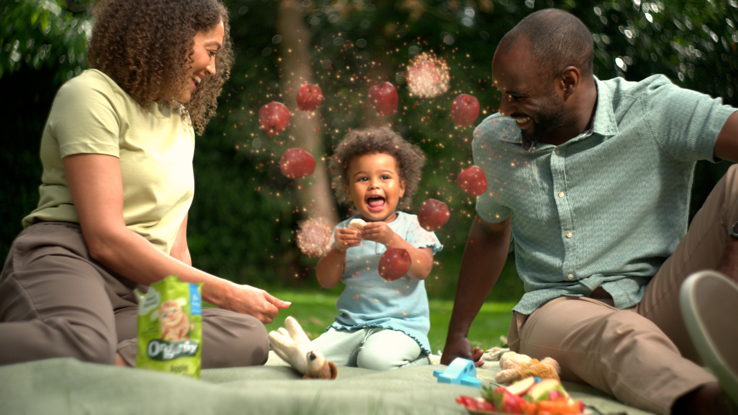 Mum dad and baby on a picnic blanket baby enjoys Organix food and experiences a rainbow burst of flavour